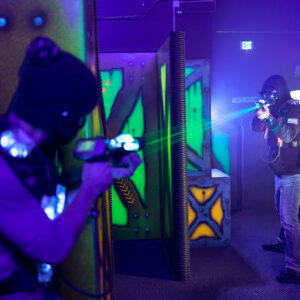 Two people playing laser tag in an arena zapping each other from across the room with the bright green auora laser.