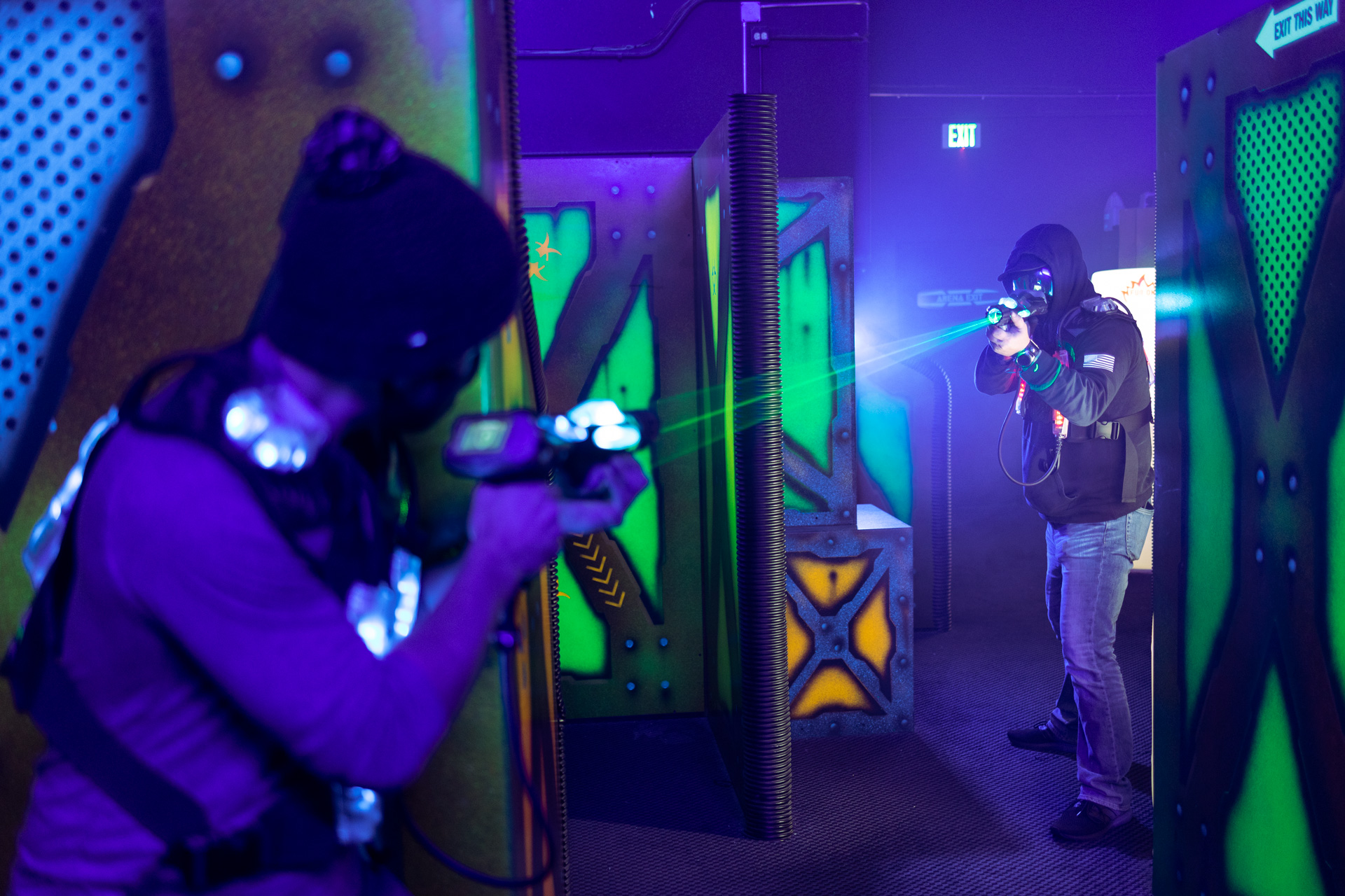 Two people playing laser tag in an arena zapping each other from across the room with the bright green auora laser.