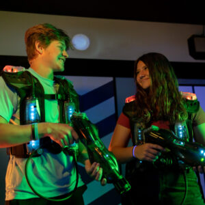 Boy on left, girl on right, looking at each other wearing laser tag equipment.