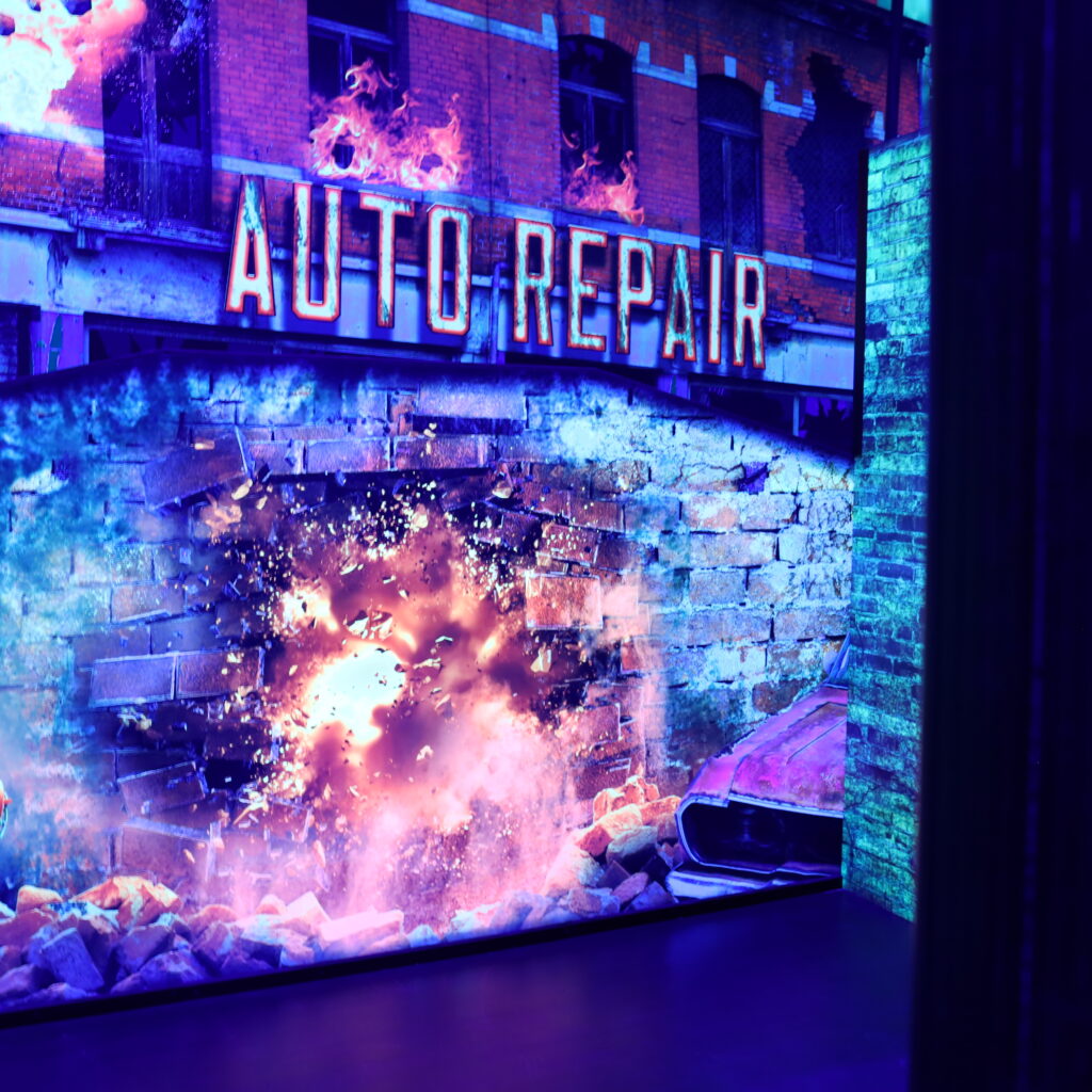 Laser Tag arena graphic displaying an explosion coming though a brick wall with a sign above it displaying "Auto Repair"