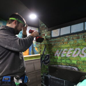 Man installing a game start button in a laser tag vesting room.
