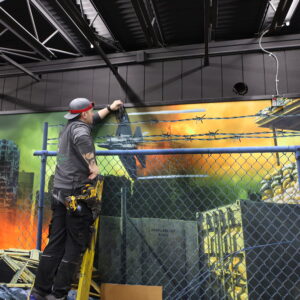 Man on a ladder setting up cabling for laser tag equipment in an arena.