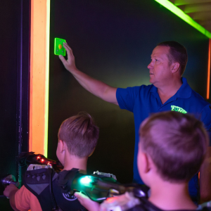A man pushing a button on the wall while two kids walk into a laser tag arena.