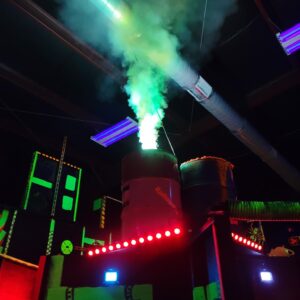 Barrel with smoke coming out of the top and a red par light below it in a laser tag arena.