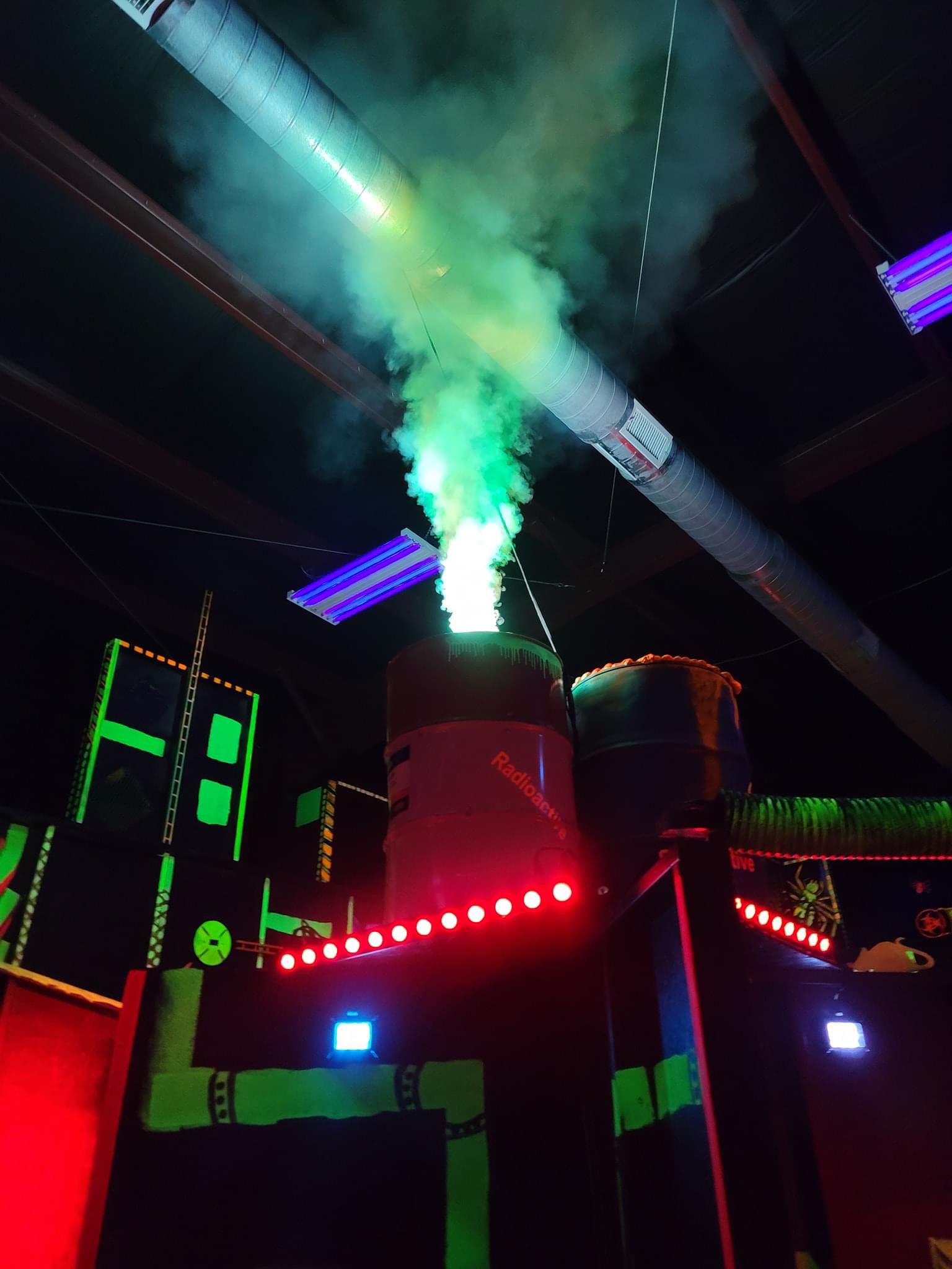 Barrel with smoke coming out of the top and a red par light below it in a laser tag arena.