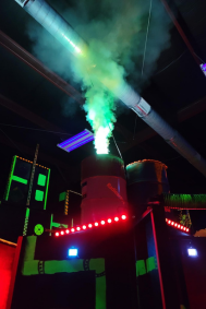 Barrel on a platform in a laser tag arena with fog coming out of the top and a red bar light near the bottom.
