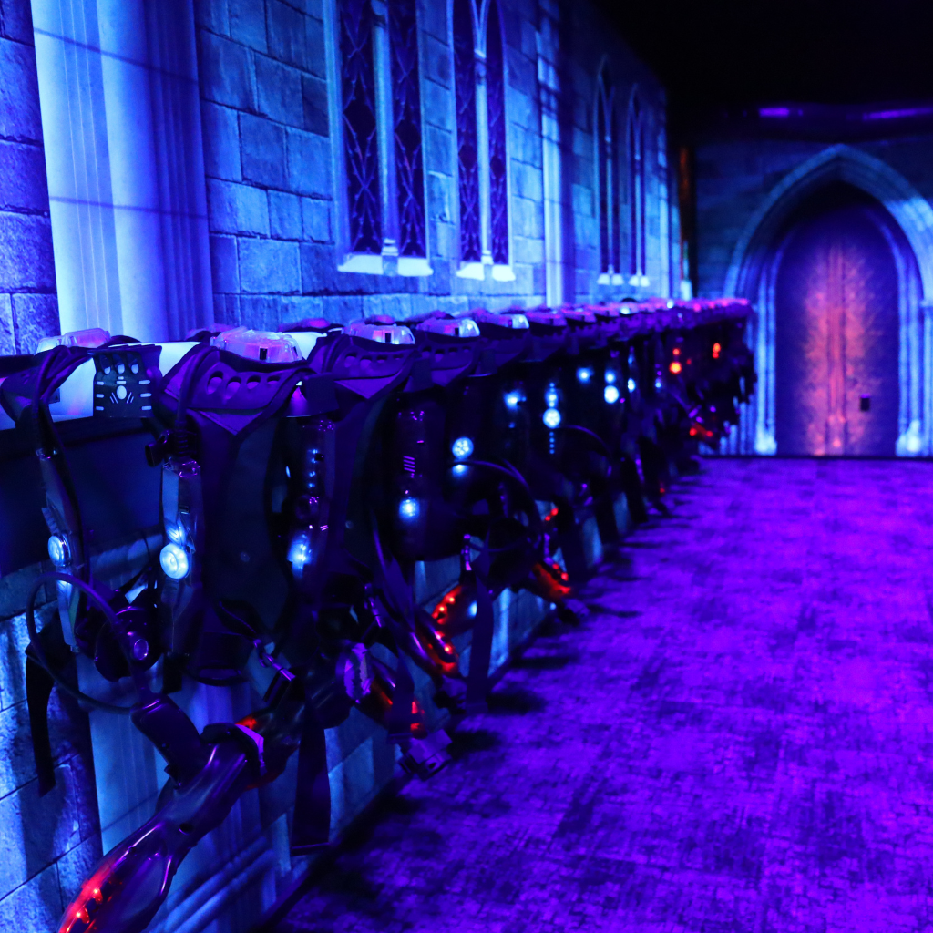 Laser tag vests hanging in a row on wireless charging racks in a laser tag arena.