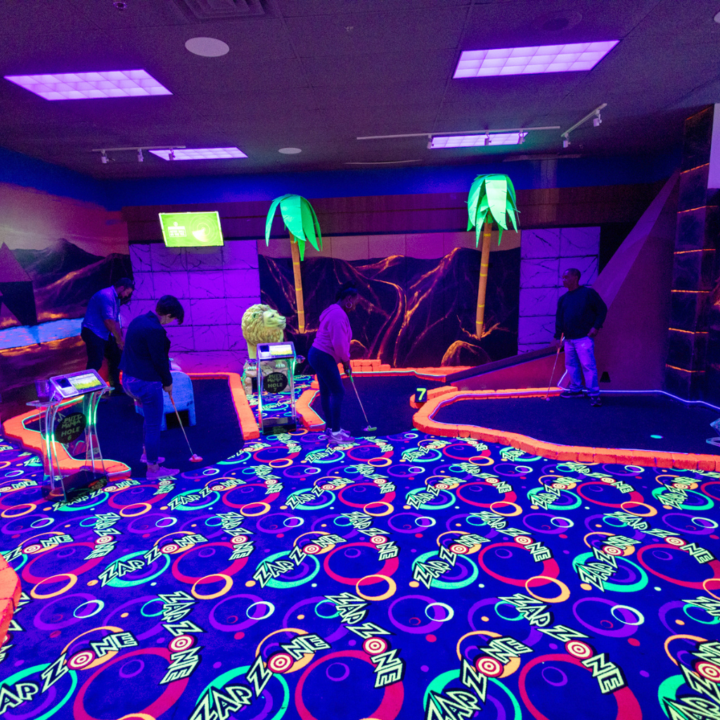 Multiple people playing on an indoor glow golf mini golf course.