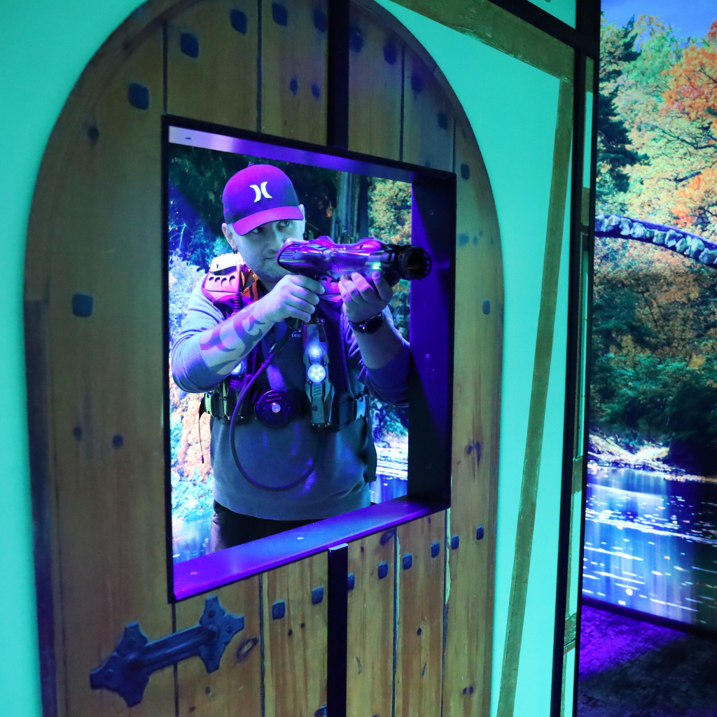 Man aiming a laser tag phaser through an opening in a prop door.