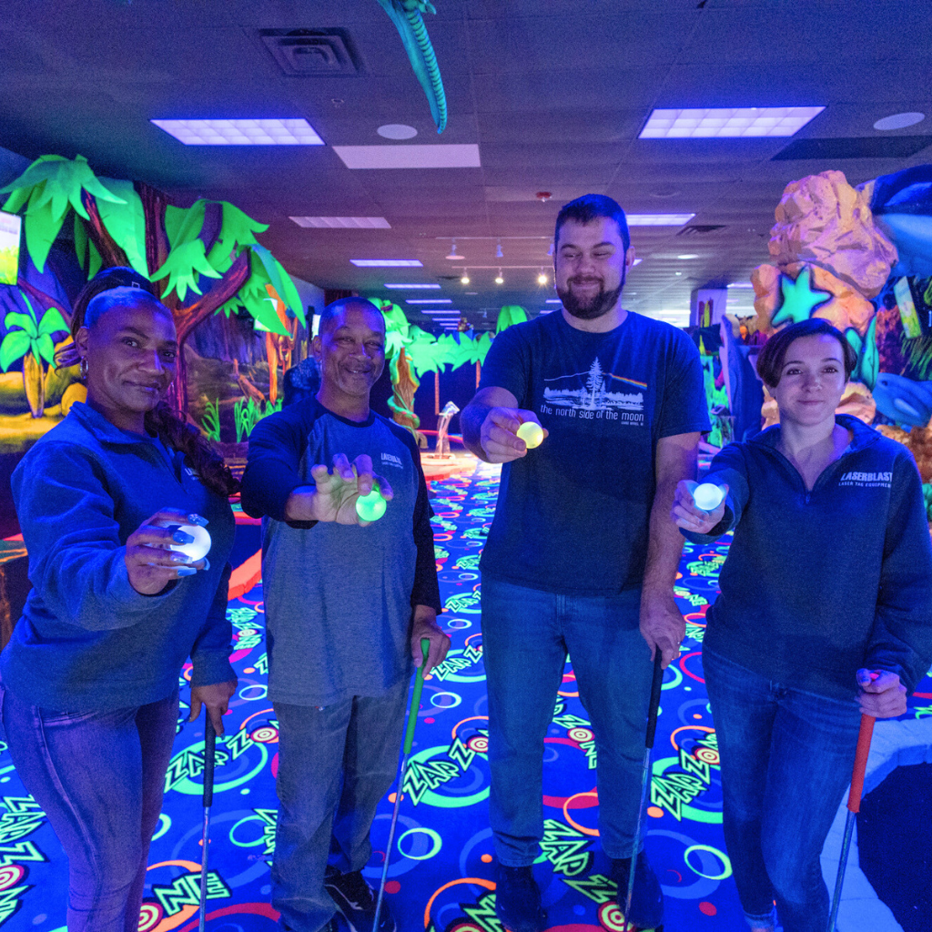 Four people standing in a row and holding out light up Putt Mania golf balls in front of them.