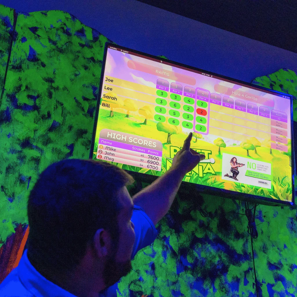 Man pointing at a Putt Mania interactive mini golf scoreboard.